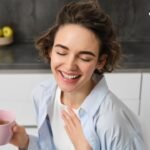 Person holding a pink mug and touching their chest while wearing a light blue shirt
